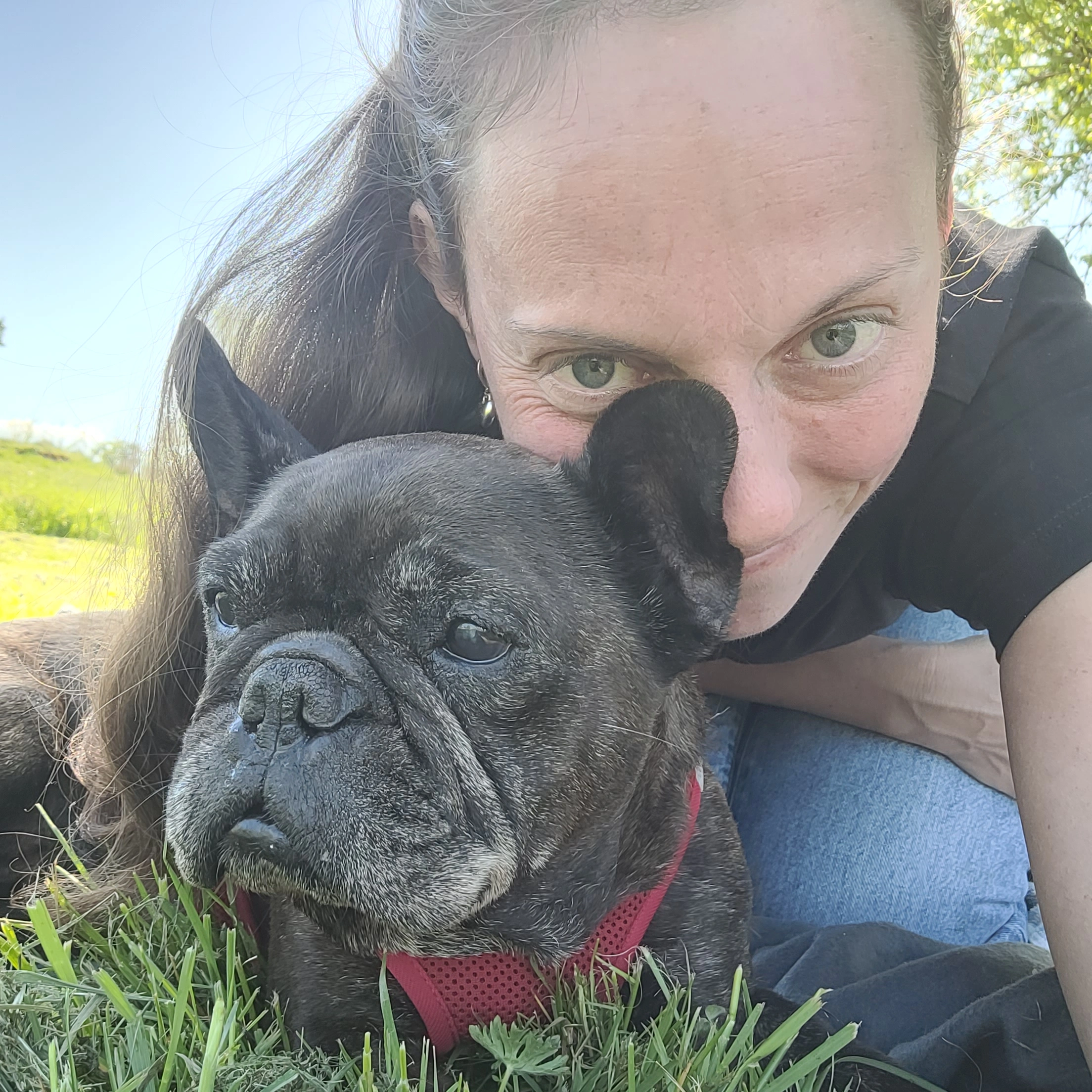 Frau liegt mit ihrem Hund in der Wiese und kuschelt